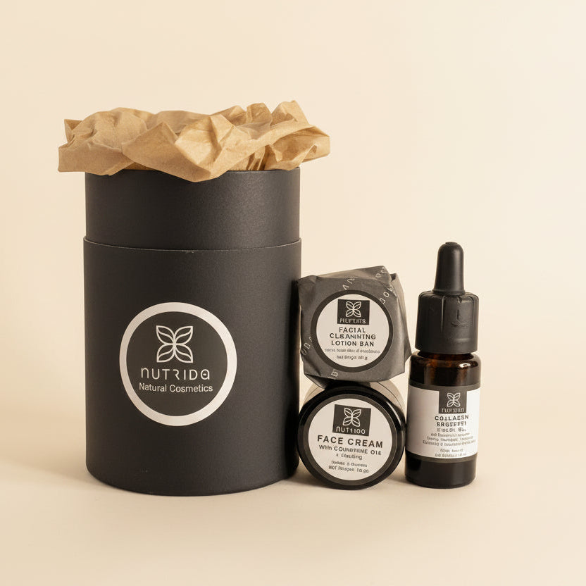 A skincare gift set from Nutida Natural Cosmetics, featuring a large matte black cylindrical box with a brown paper tissue insert, alongside two small round jars of face cream and a small amber dropper bottle, all with white labels and black caps, arranged on a warm beige background.