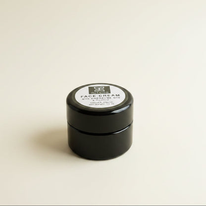 A small black plastic jar of Nutrido Face Cream with Coenzyme Q10 and Rosehip, resting on a textured white fabric background.