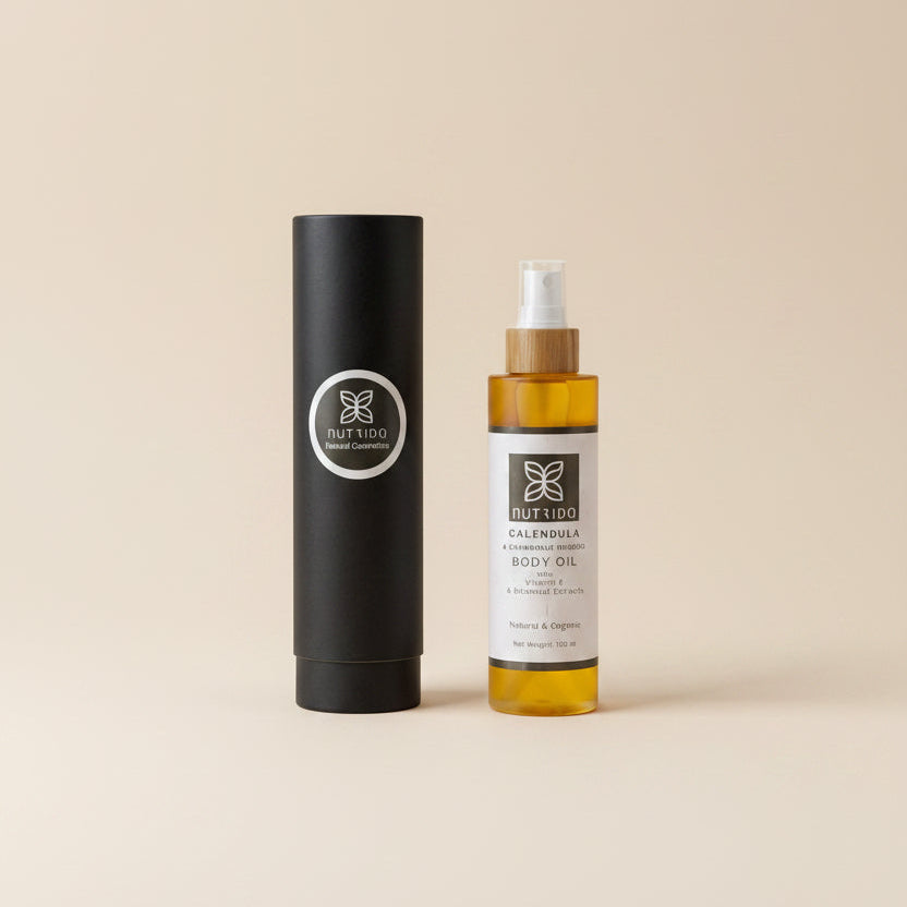 A bottle of Fuller's Calming Body Oil with a white label and amber liquid, placed next to its black cylindrical cardboard packaging on a textured white fabric background.