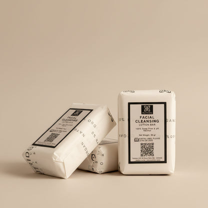Four wrapped facial cleansing lotion bars arranged on a light fabric surface, with one bar standing upright and three lying down. The packaging is cream-colored with black text and small floral line drawings.