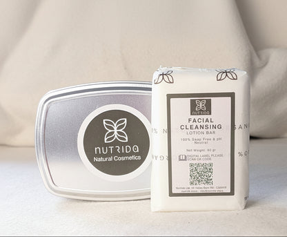 A packaged facial cleansing lotion bar standing upright next to its silver tin container on a soft beige fabric surface. The front label reads 'NUTRIDQA Natural Cosmetics' and 'FACIAL CLEANSING LOTION BAR'.