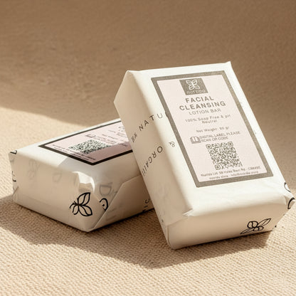 Two wrapped facial cleansing lotion bars on a beige surface, with the front package clearly showing the label 'Facial Cleansing Lotion Bar' and a QR code. The brand name appears as 'NATURE' with a butterfly-like logo.