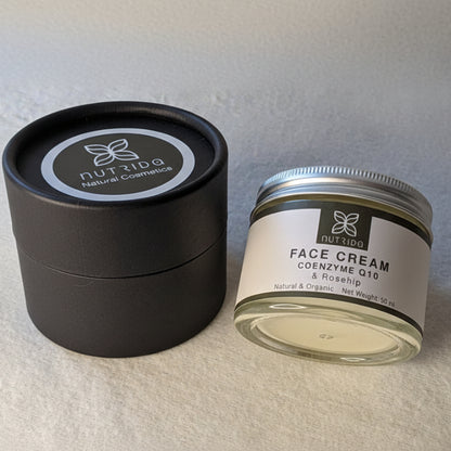 A jar of Nutrida Natural Cosmetics Face Cream next to its black circular lid on a textured light gray fabric background.