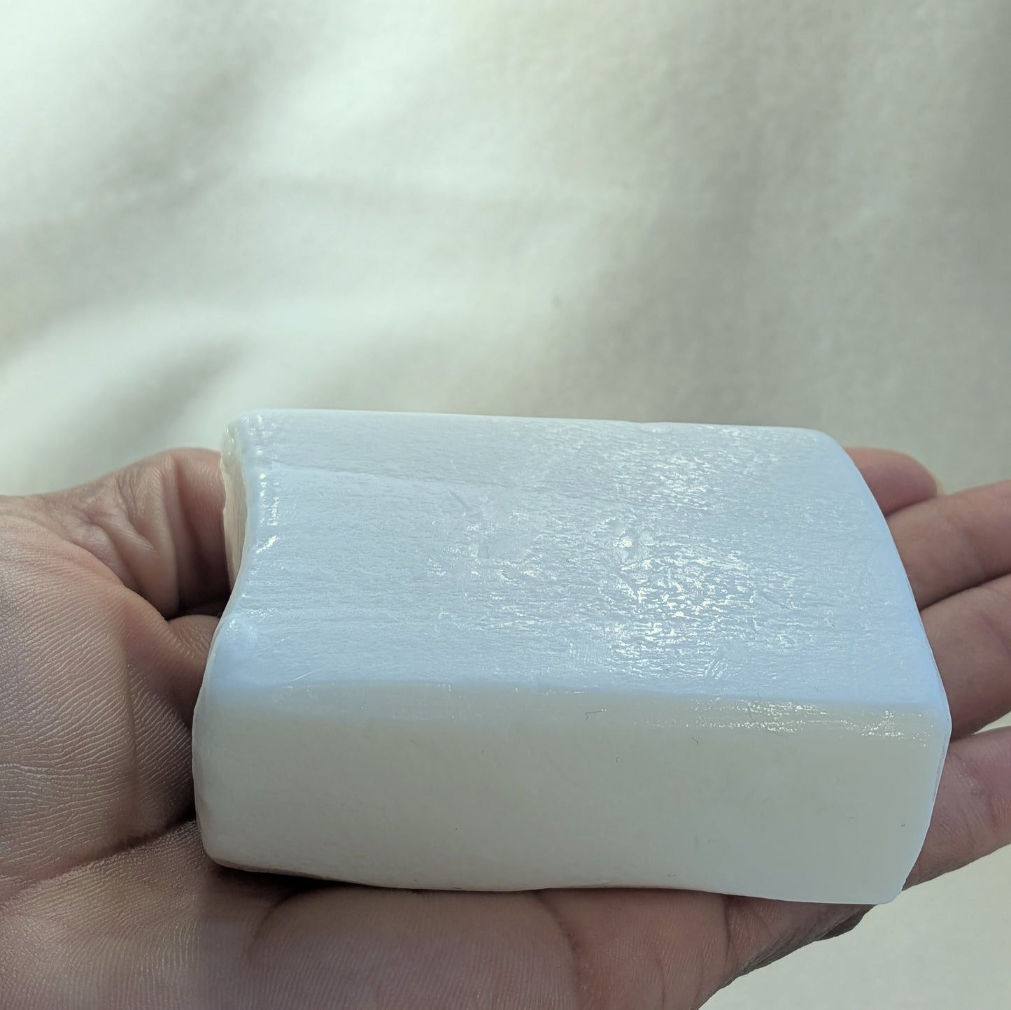 White bar of soap held in a hand against a neutral background