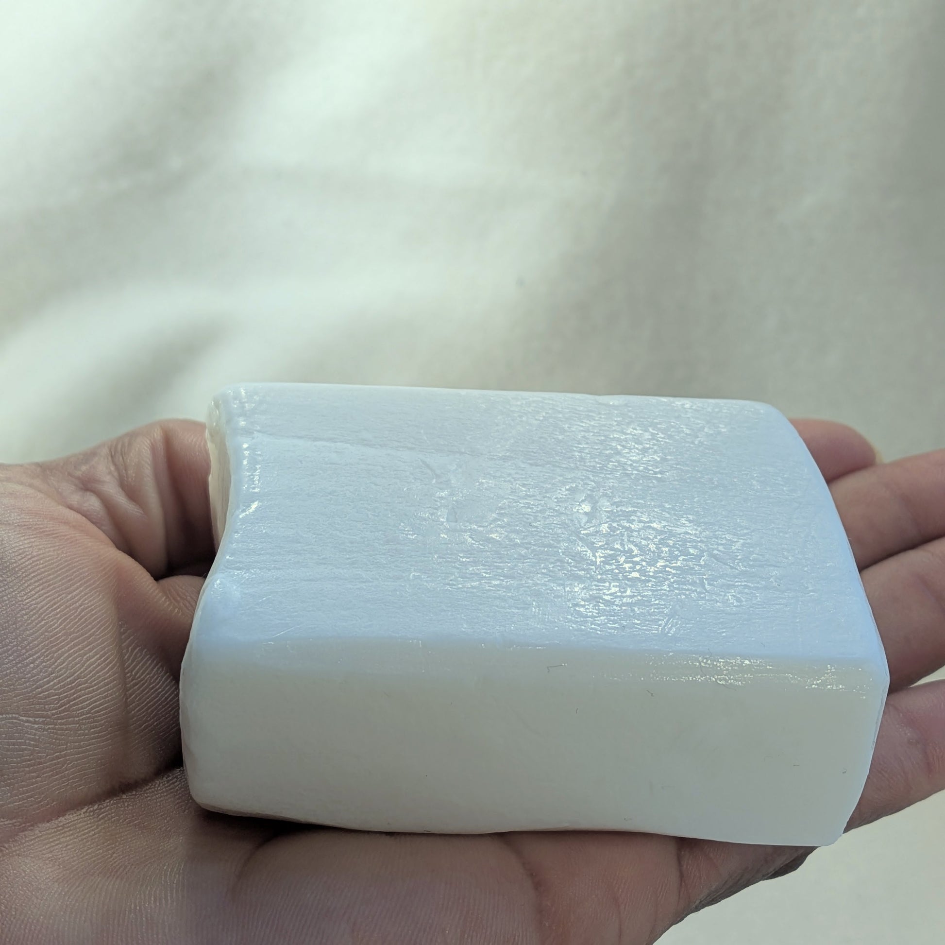 White bar of soap held in a hand against a neutral background