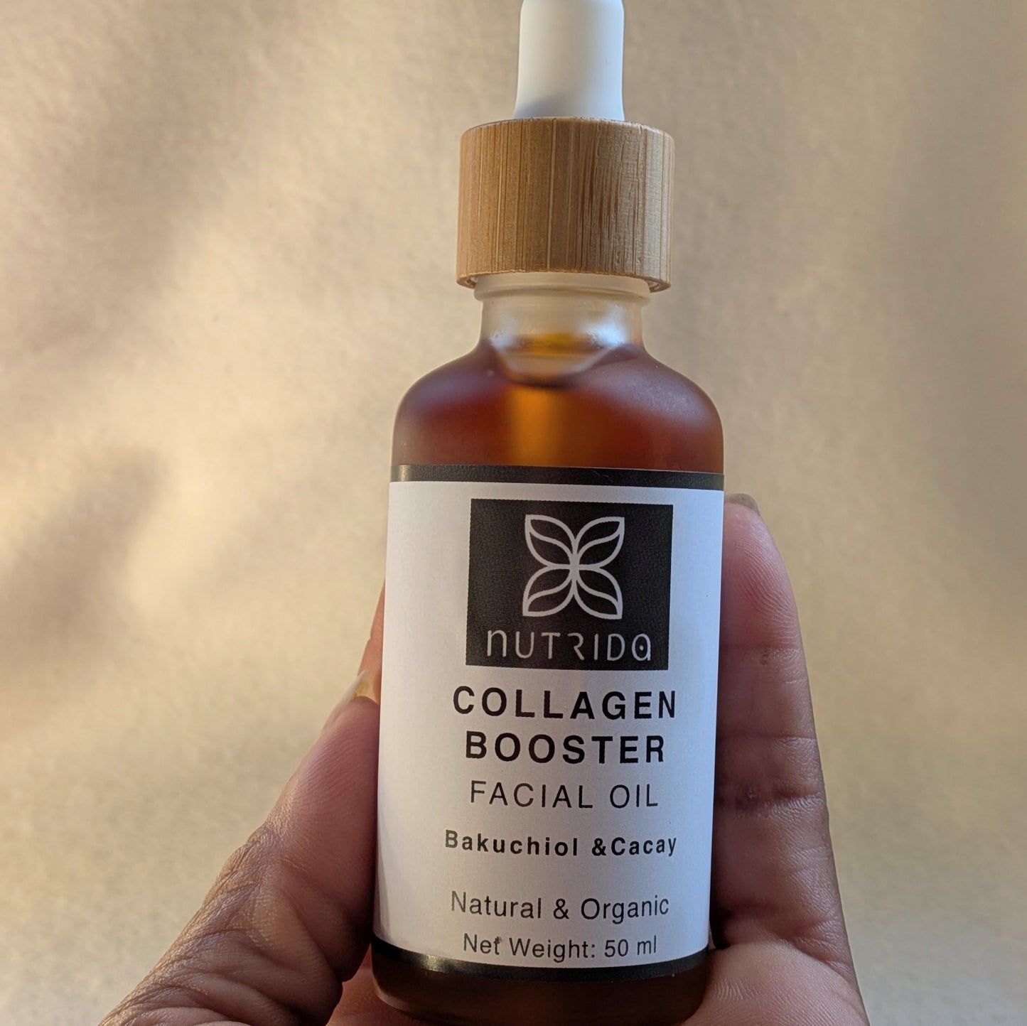 Bottle of Nutrida Collagen Booster Facial Oil held in a hand with a neutral background
